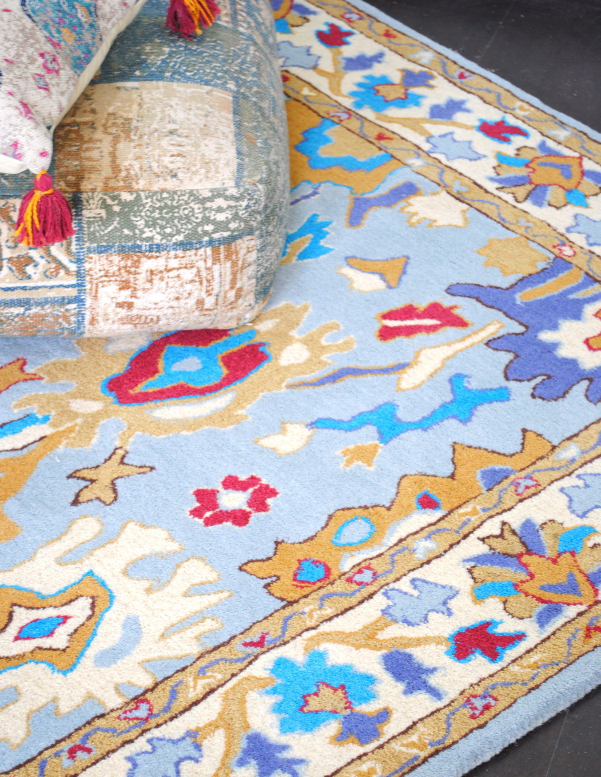 Agra hand-tufted wool rug, angled view of the sky-blue field with turquoise, ochre and madder red palmettes and ivory floral border