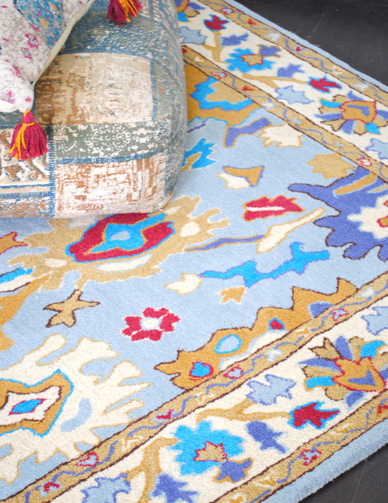Agra hand-tufted wool rug, angled view of the sky-blue field with turquoise, ochre and madder red palmettes and ivory floral border