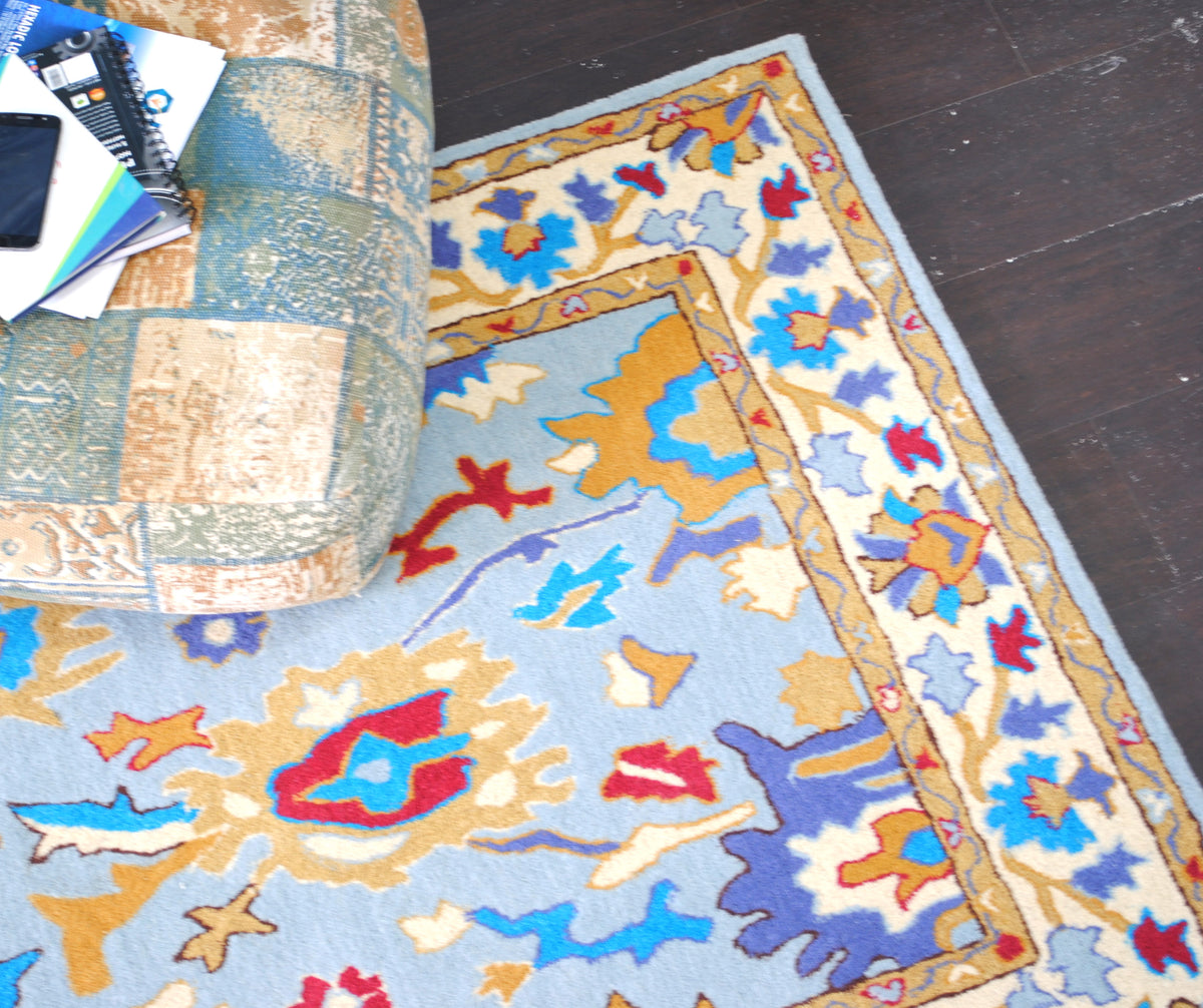 Corner of the Agra rug from above, ivory border of turquoise, periwinkle and red flowers between ochre guard stripes