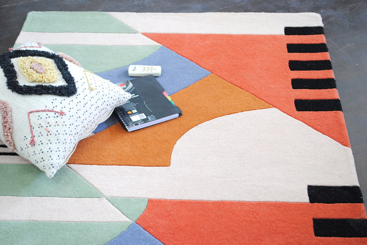 Goa hand-tufted wool rug laid on a dark floor, styled with a tufted floor cushion, coral field and black bars along the right edge, Art Avenue