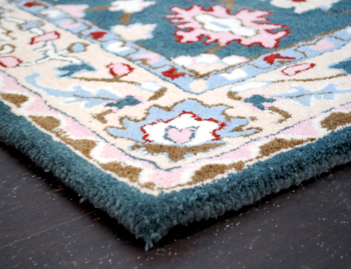 Corner of the Srinagar rug: dense sheared wool pile, cream vine border and teal wool-bound edge with no fringe