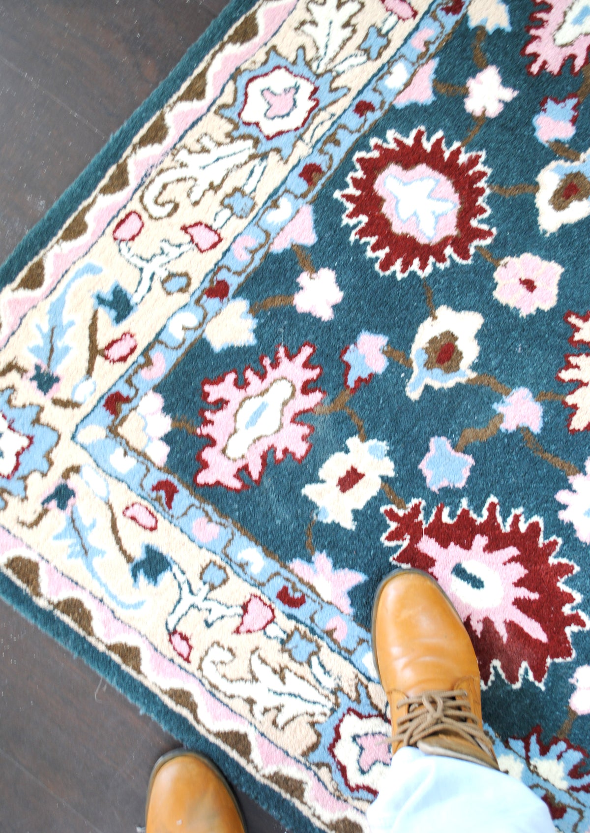 Corner of the Srinagar wool rug from above, showing the border layers and the teal floral field, feet for scale