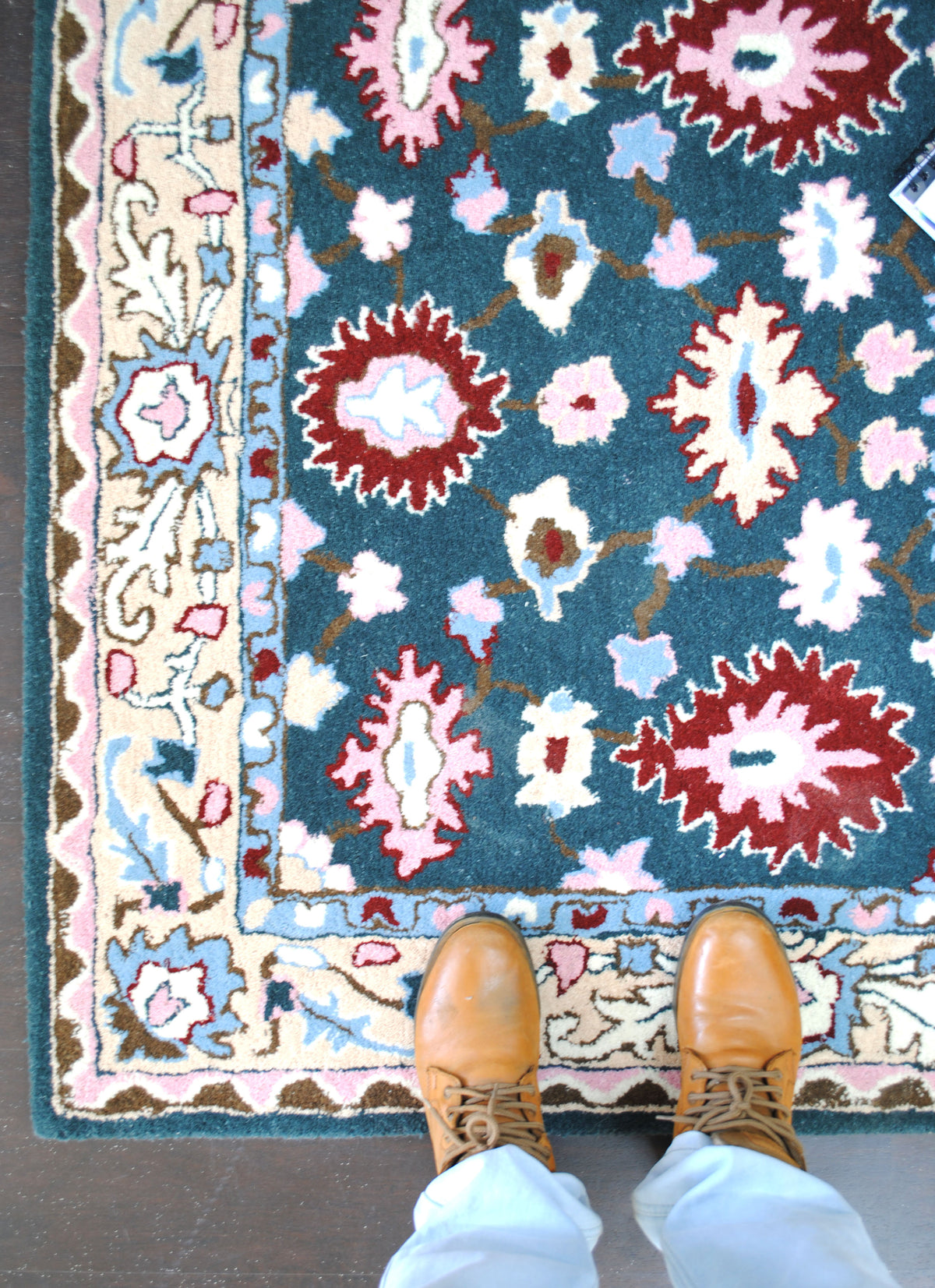 Standing on the Srinagar hand-tufted rug, showing the scale of the crimson rosettes and the width of the cream border
