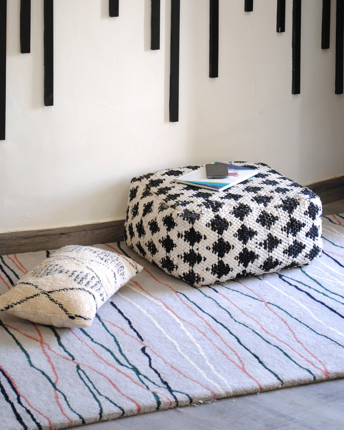 Chilika grey abstract wool rug on the floor with a woven black-and-white pouf and a textured cushion