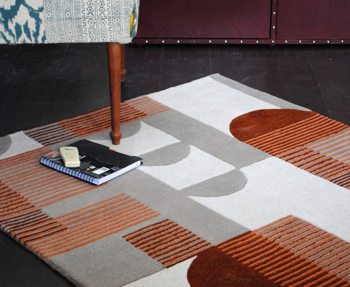 Ahmedabad geometric wool rug on a dark wood floor beside an upholstered armchair and a studded cabinet
