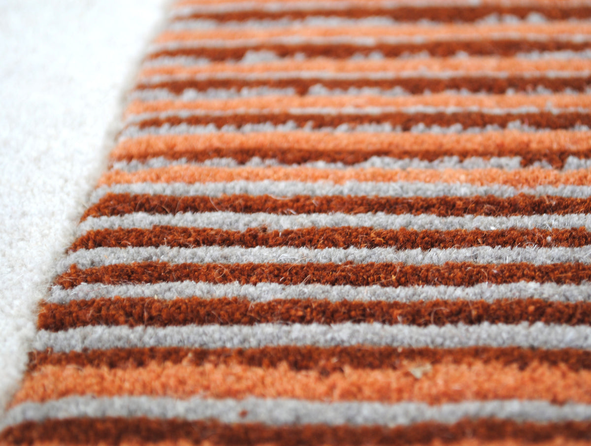 Macro of hand-tufted New Zealand wool stripes in burnt orange and rust on stone grey