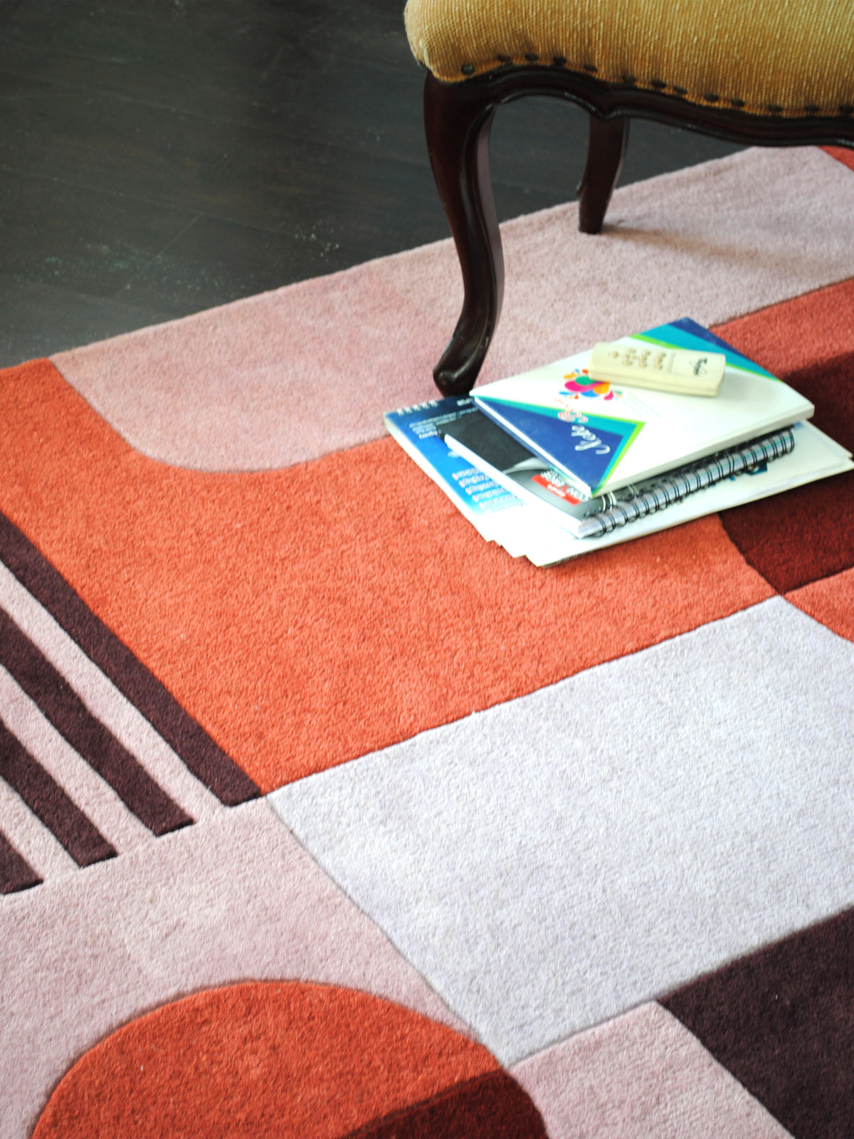 Konark rug beneath a carved wooden chair, terracotta panel and plum pinstripes beside a split disc