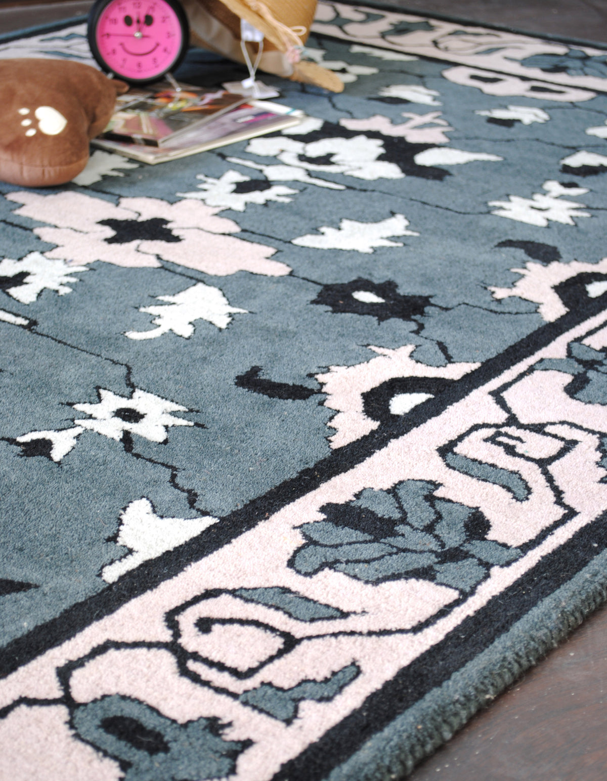 Angled view of the Shimla rug's blush border with slate palmettes and black scrolling vine beside the floral field