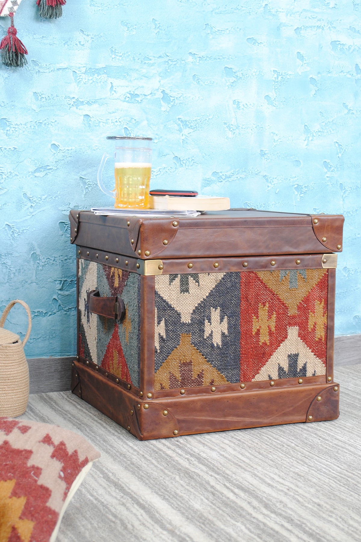 Madras leather-top kilim trunk in three-quarter view with a woven basket and kilim cushion