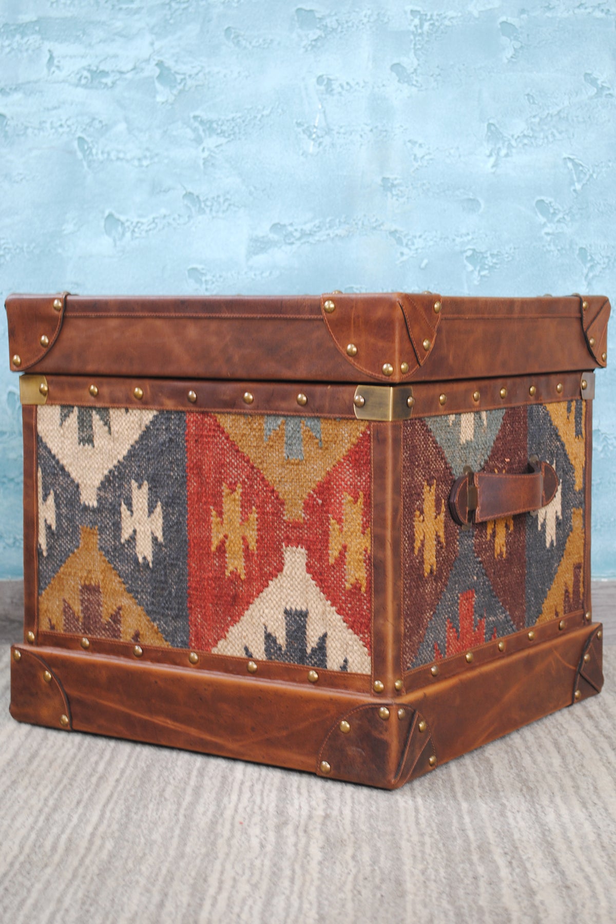 Madras kilim trunk in three-quarter view with the leather strap and brass turning catch visible
