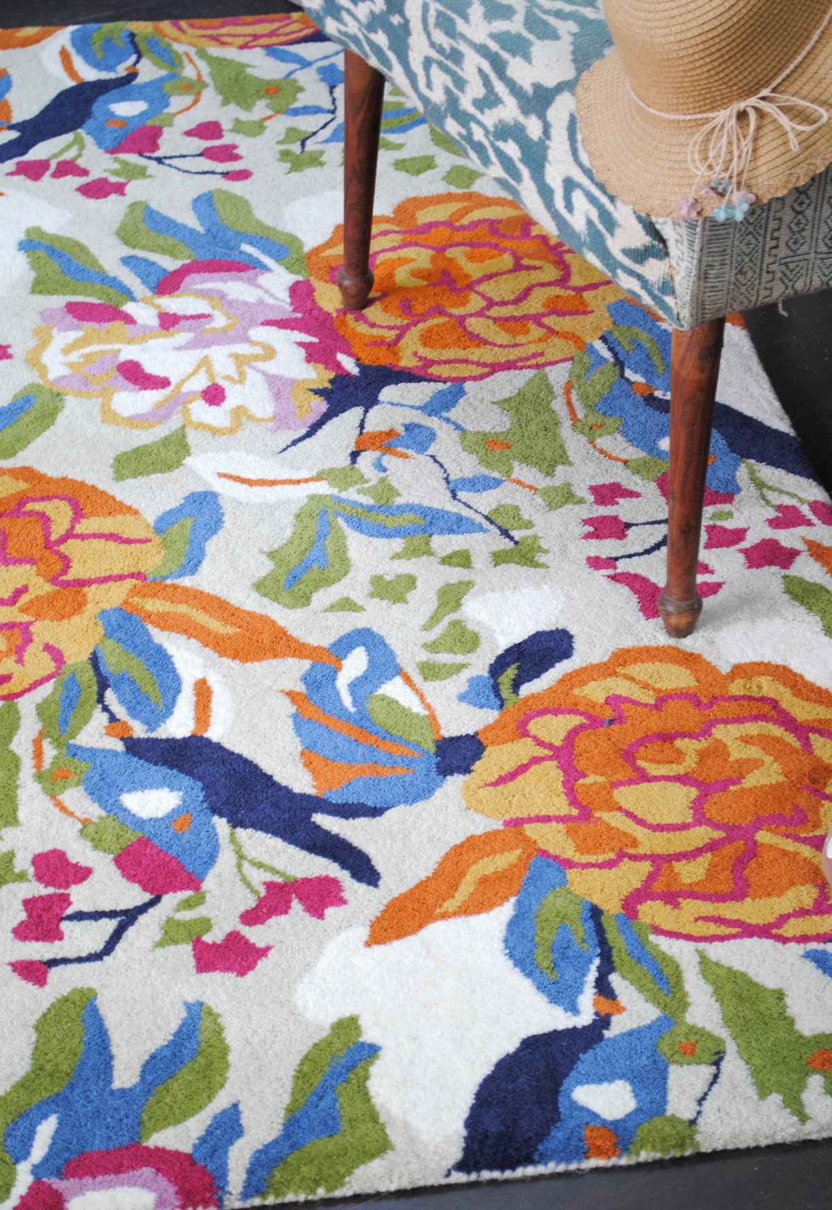 The Ooty rug from above beside the legs of an ikat chair, showing orange and marigold peonies, fuchsia sprigs and navy and cornflower birds