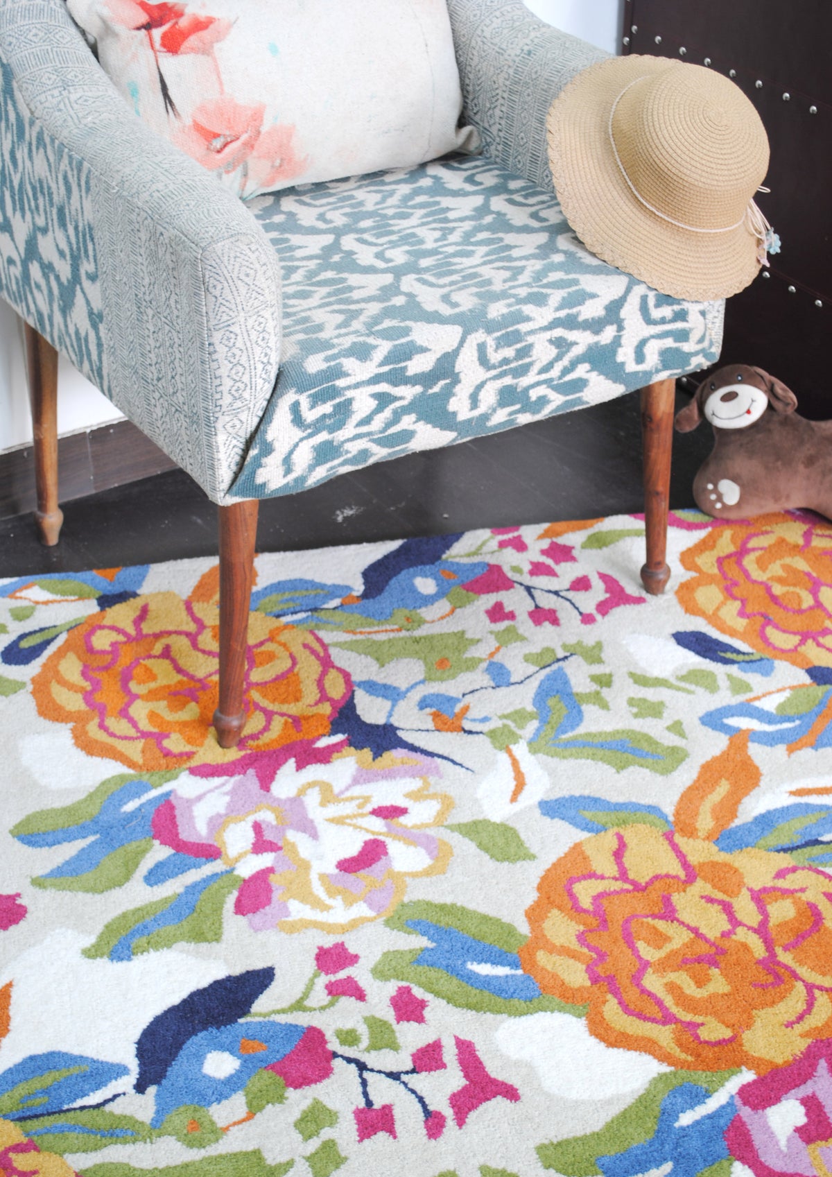 Looking down at the Ooty rug beneath an ikat armchair: orange peonies, lilac and white blooms and blue birds on a pale grey ground