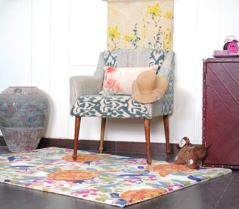 Ooty hand-tufted rug under an ikat upholstered chair on a dark wood floor, with orange peony blooms and blue birds across the field