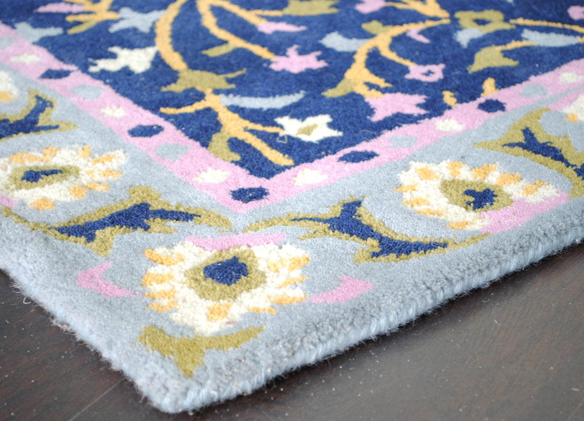 Corner of the Nishat rug showing the pink dotted guard stripe and powder-blue border blossoms