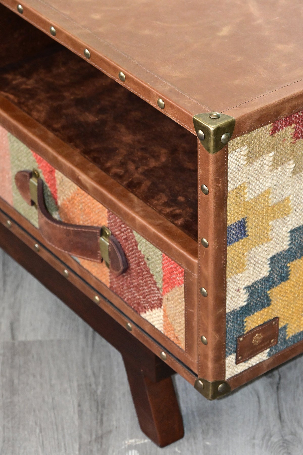 Detail of the Ranakpur TV unit's corner, brass corner cap, domed studs, leather strap handle and kilim flank
