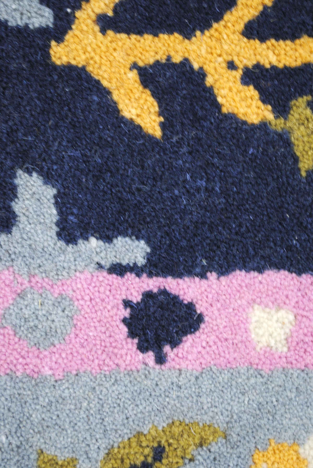 Macro of the hand-tufted wool pile: saffron vine, navy ground, pink band and powder-blue border