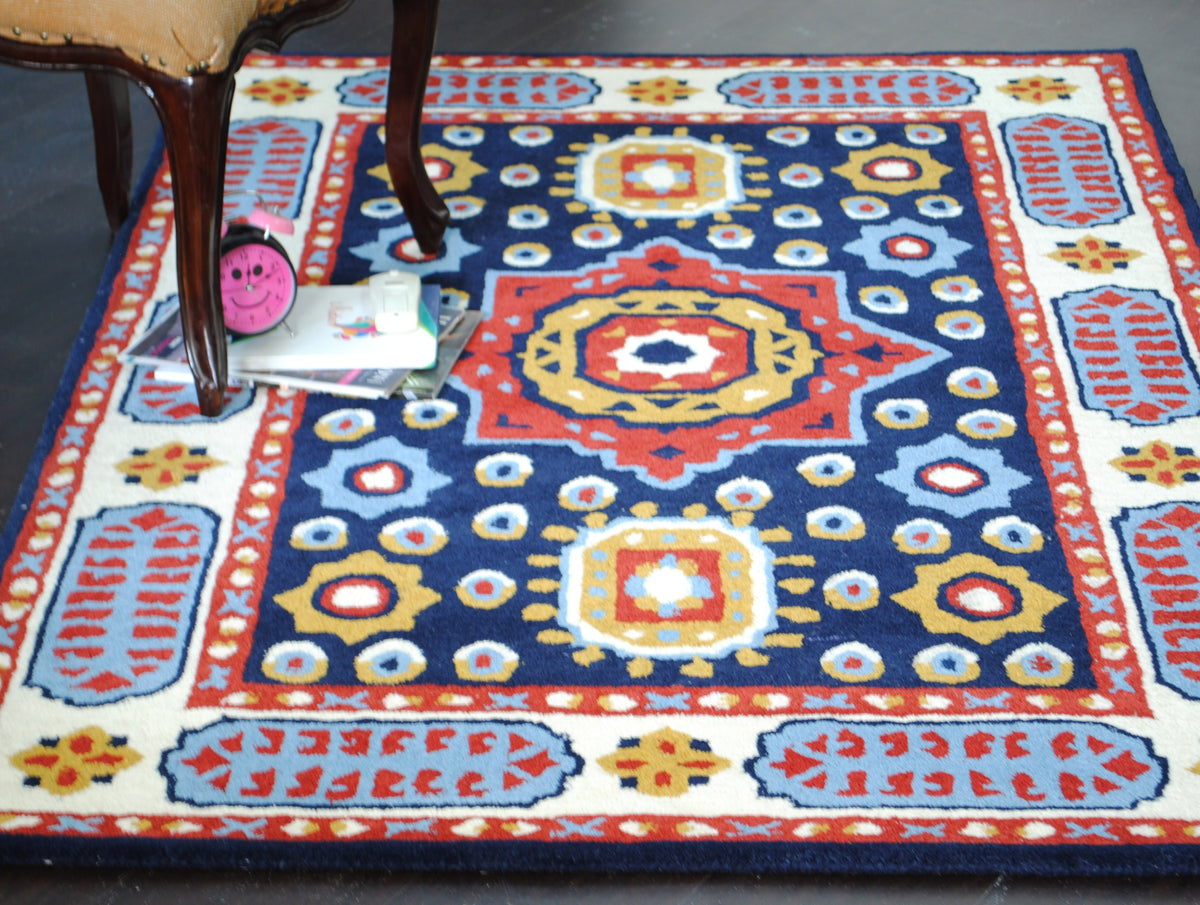 Orchha navy and red medallion rug under a carved wooden chair with books and a pink alarm clock