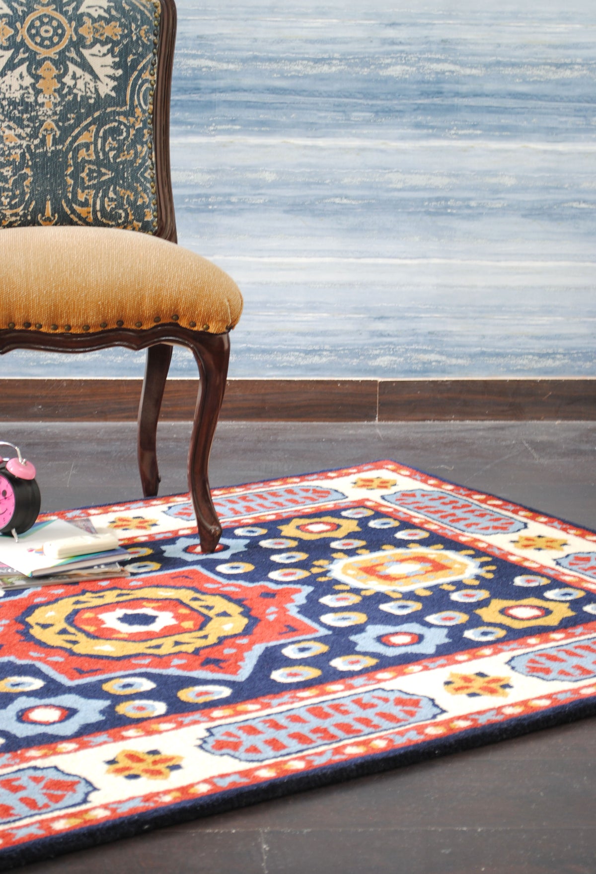 Orchha rug styled with a walnut chair upholstered in tan, against a blue-grey wall