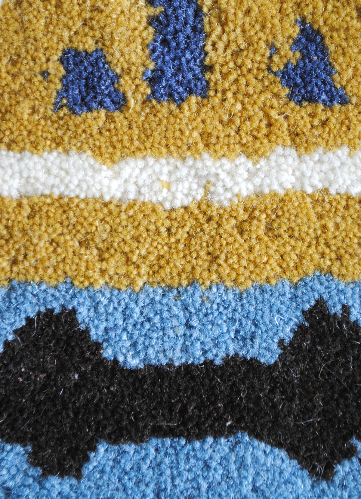Close-up of the Tawang rug's New Zealand wool pile in mustard, ivory, sky blue, cobalt and black