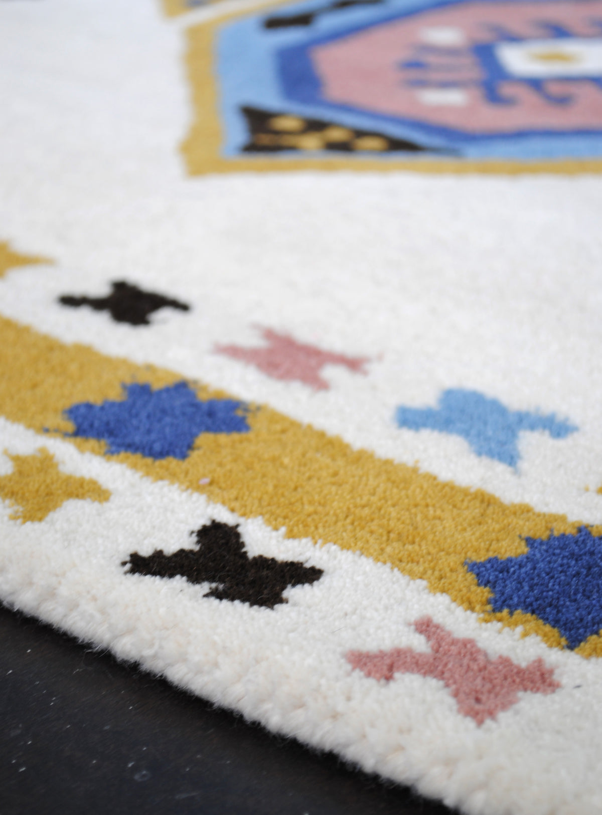 Low-angle view across the Tawang rug's mustard border of cobalt stars and ivory outer border of coloured crosses