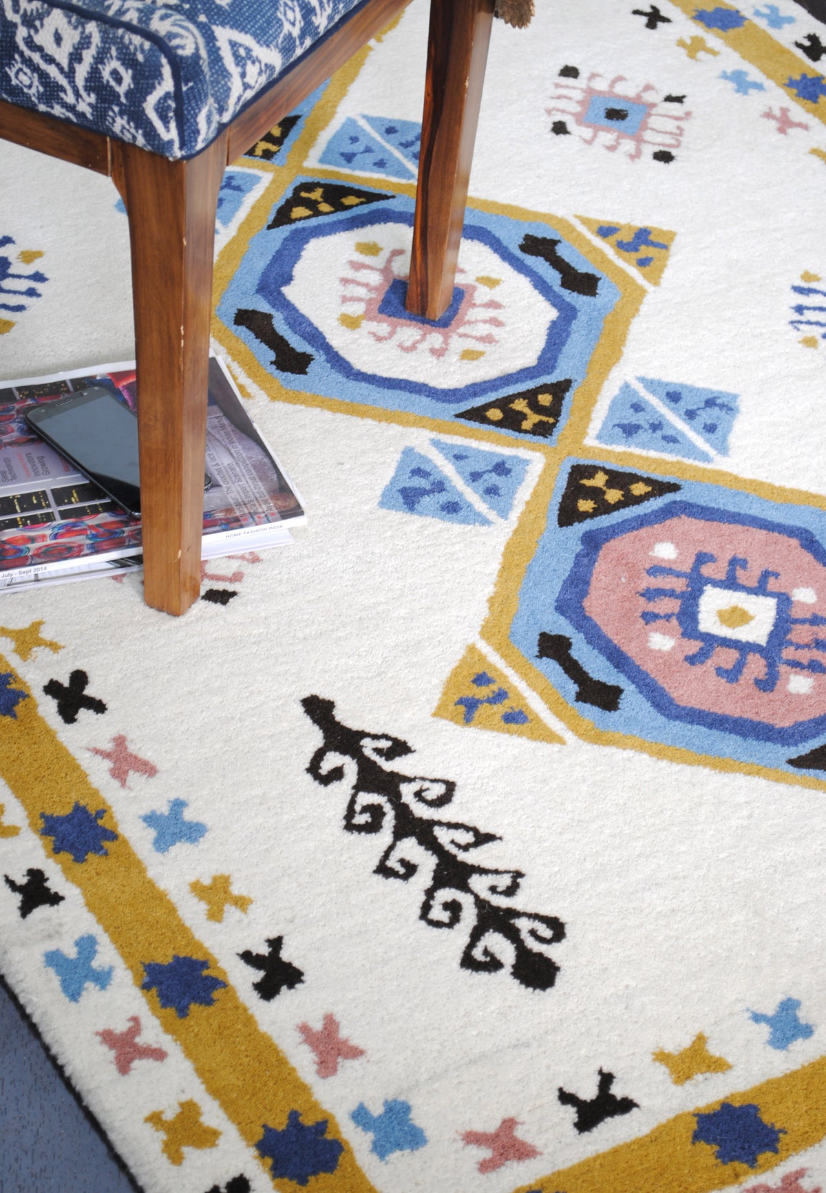Tawang rug under a wooden chair upholstered in blue print, with magazines on the ivory field