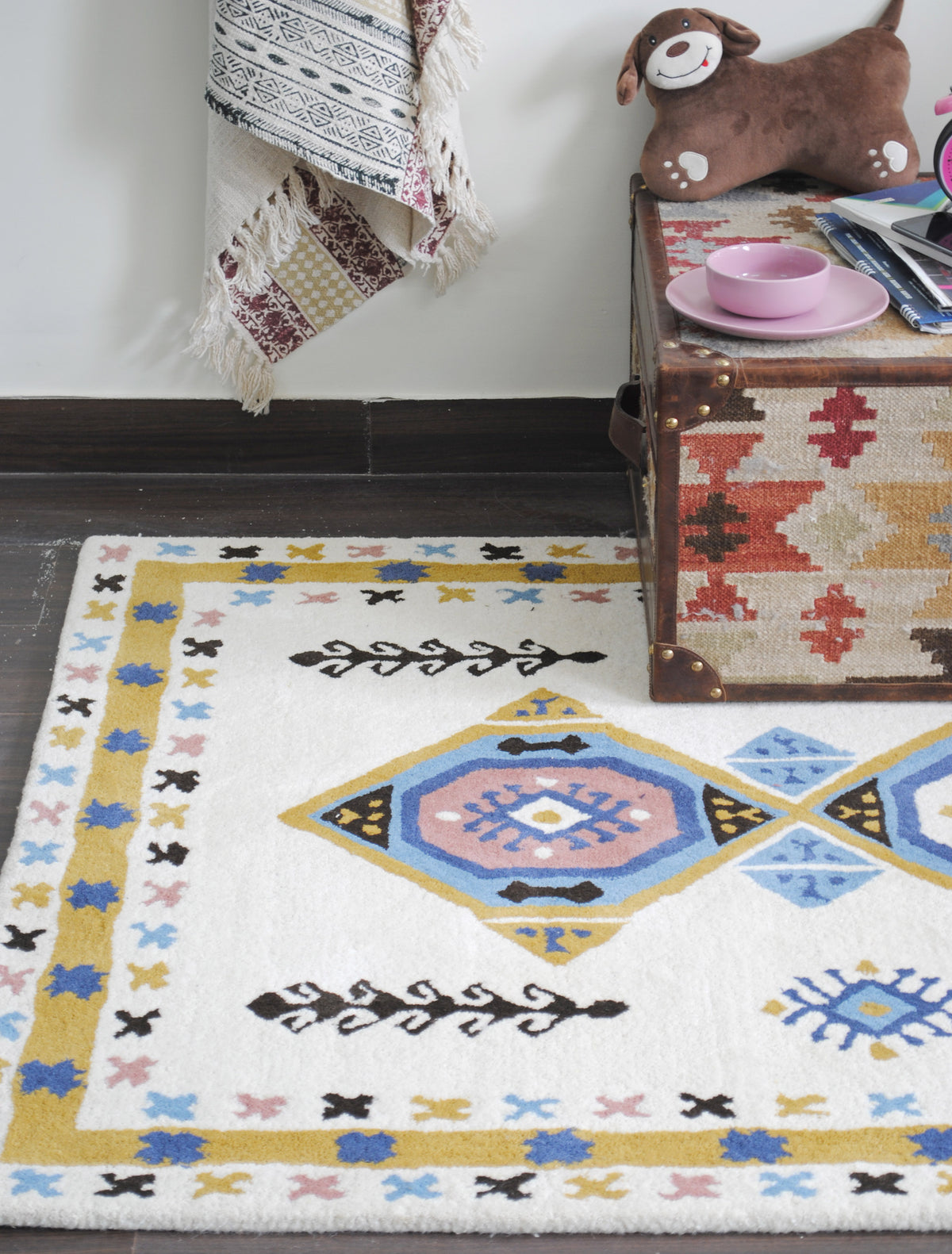 Corner of the Tawang rug showing a blush medallion, black ram's-horn vine and mustard border beside a kilim trunk