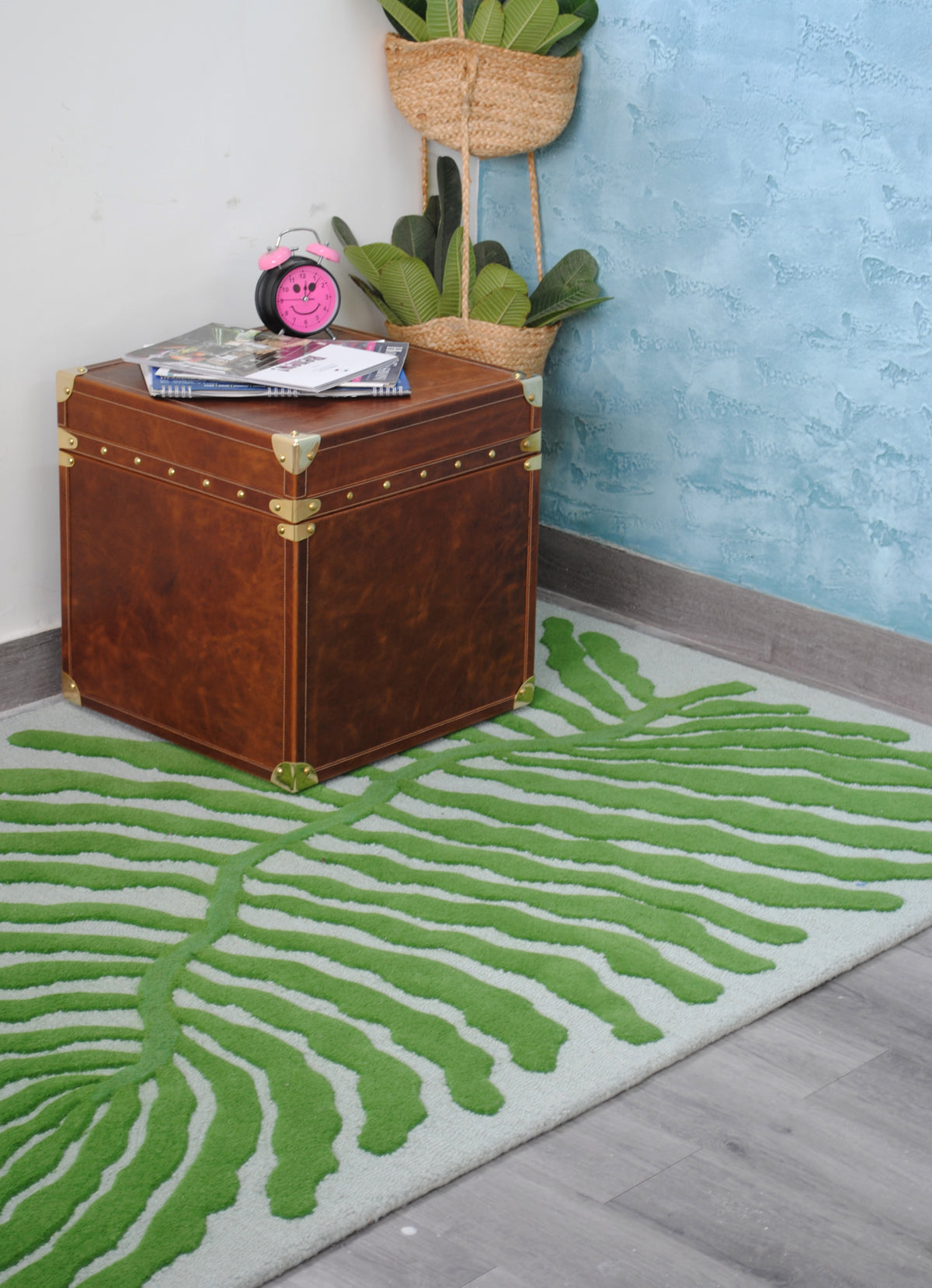 Munnar green leaf rug in a corner with the Cordoba Leather Cube Trunk, a hanging jute planter and a blue plaster wall