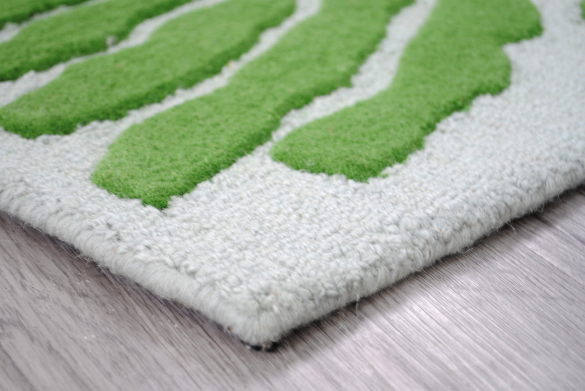 Corner of the Munnar rug showing frond tips, the loop-pile ground and the pale mint wool-bound edge, no fringe