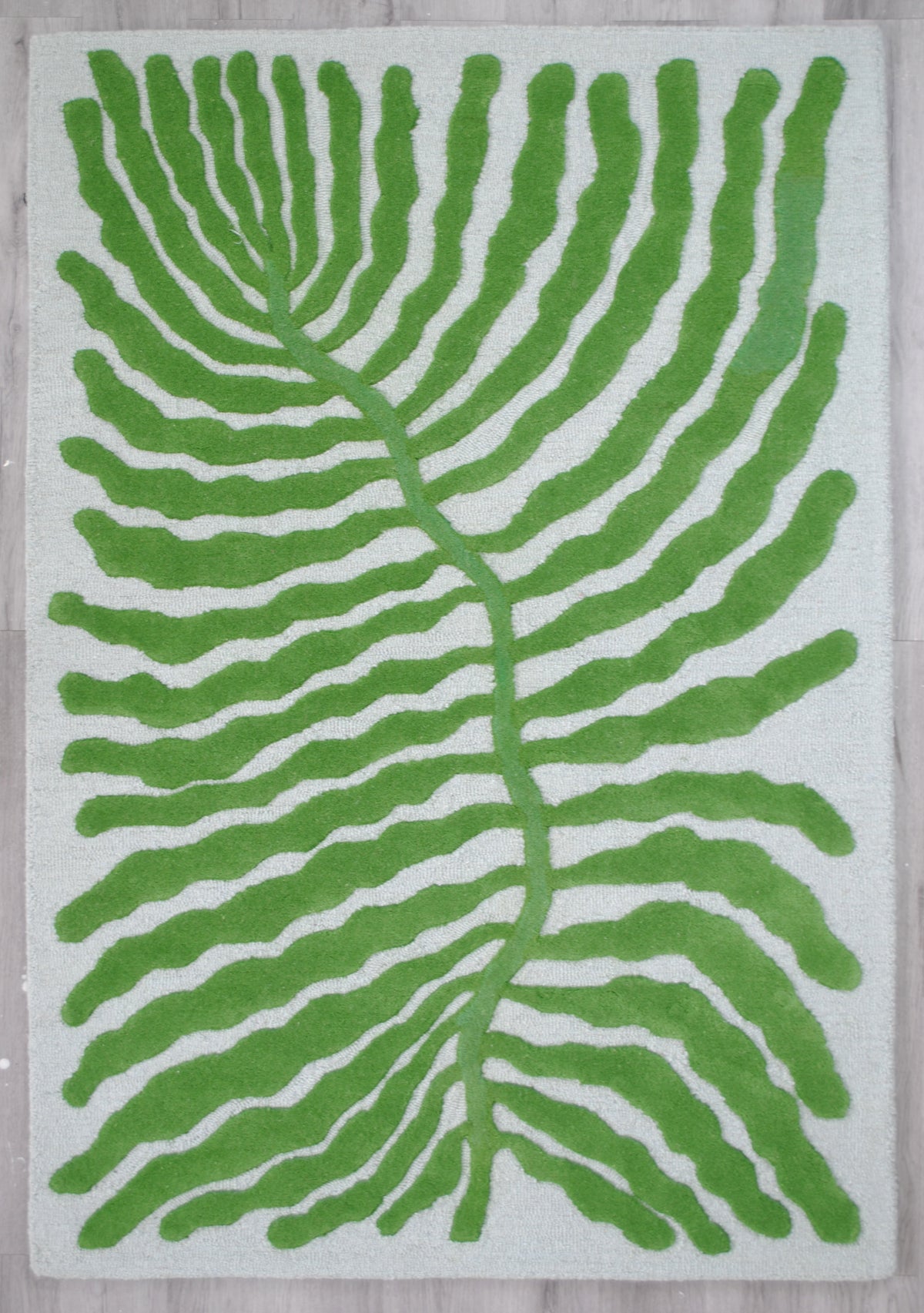 Munnar hand-tufted rug laid flat on a grey wood floor, green leaf on pale mint