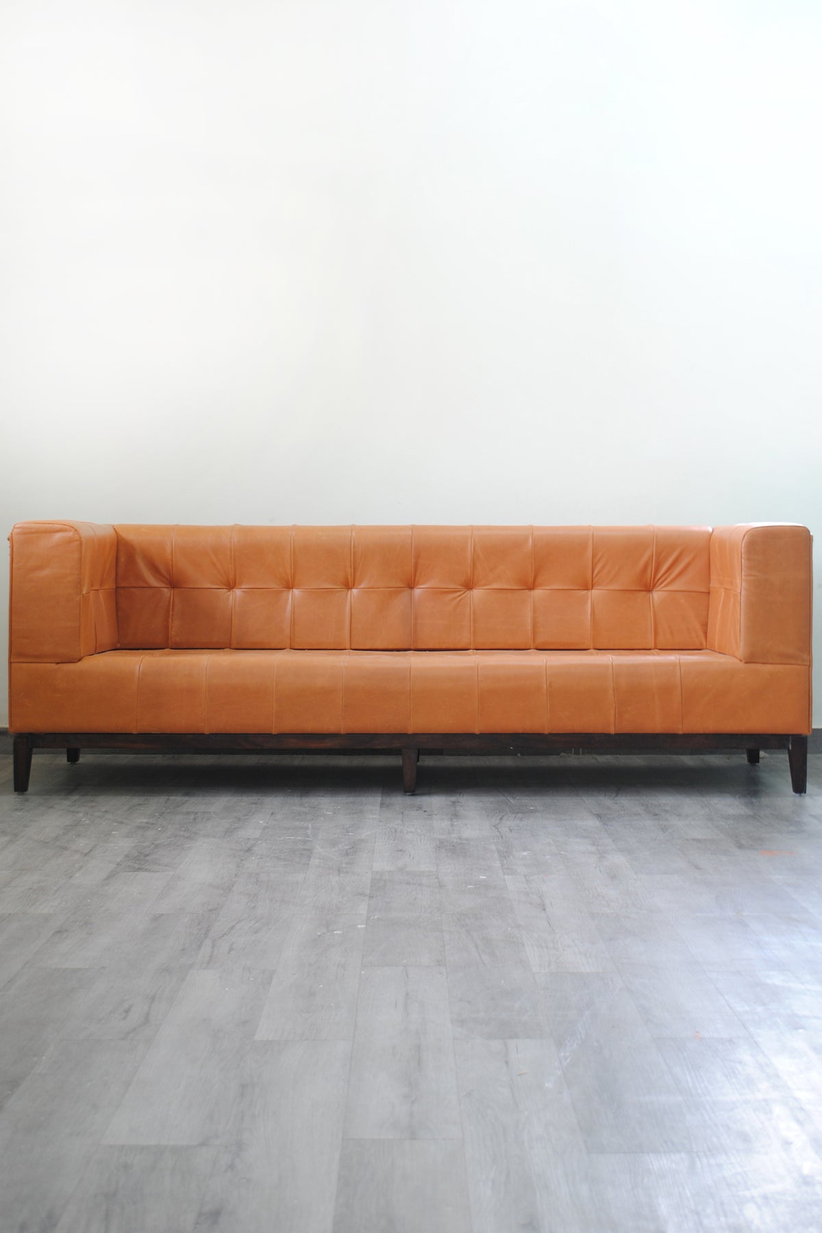 Santiago leather sofa front elevation, showing squared biscuit tufting and the solid timber plinth base