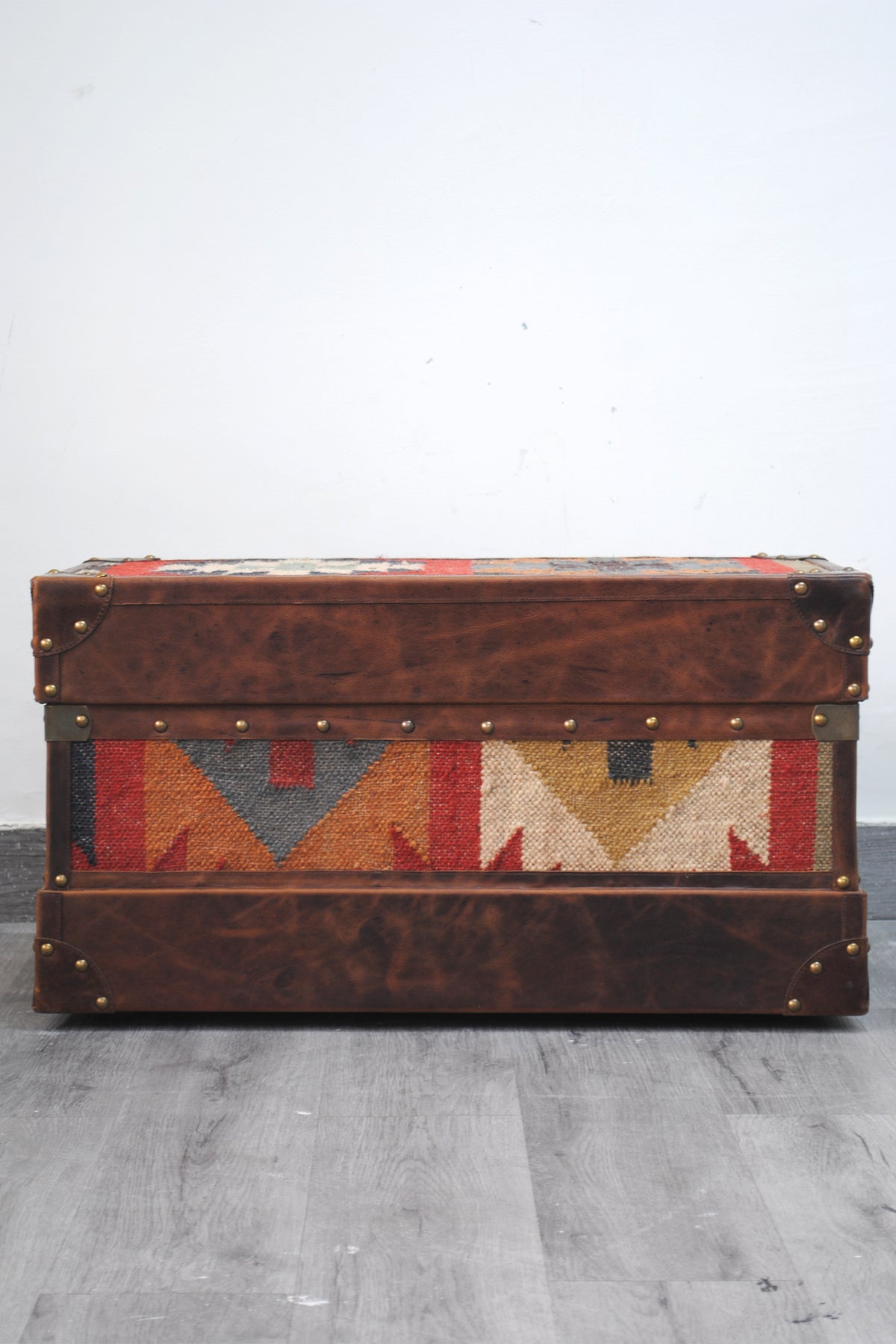 Front elevation of the Bundi kilim steamer trunk with the lid closed, showing the wide leather base band