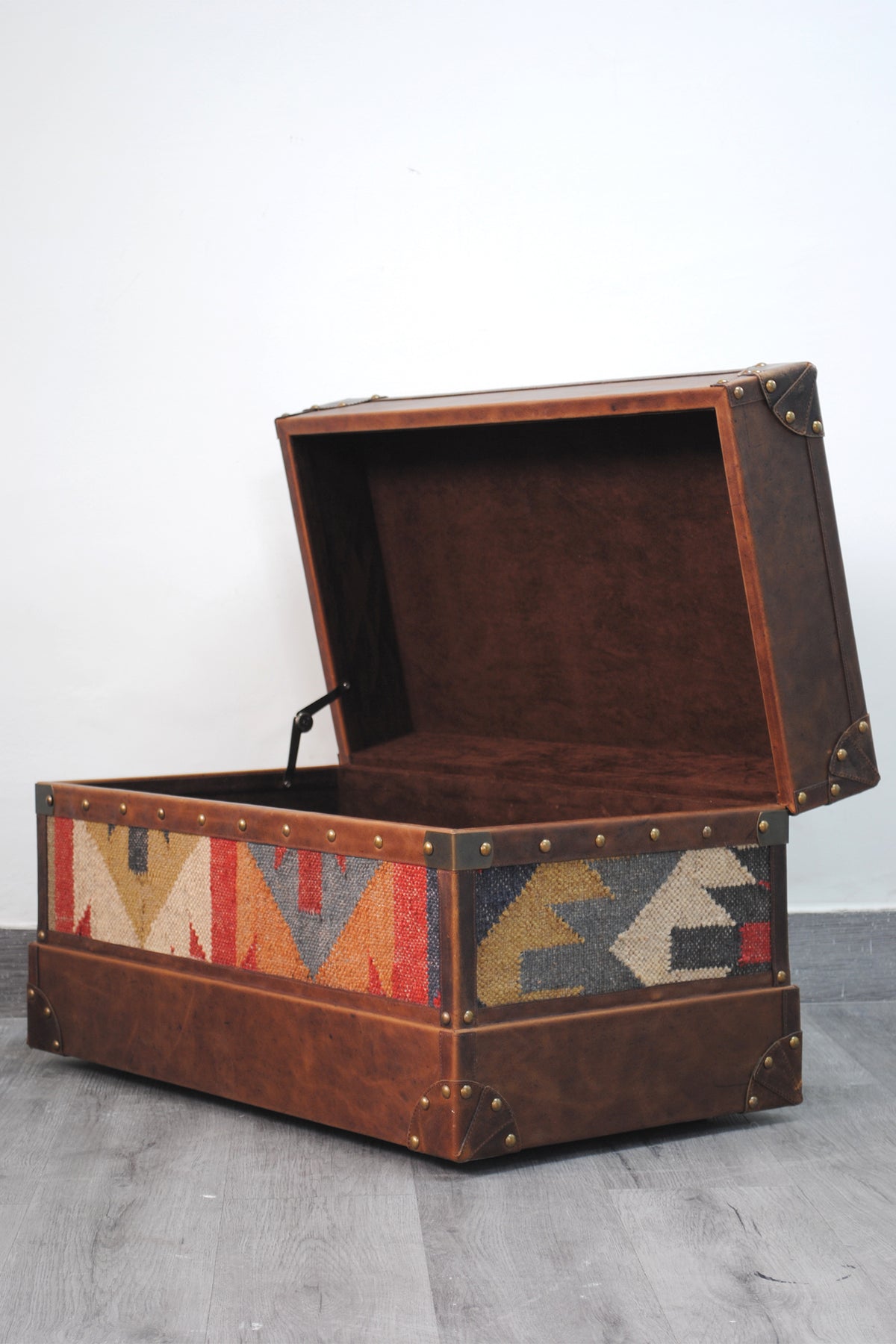 Bundi kilim steamer trunk open at an angle, showing the suede lining and steel lid stay arm