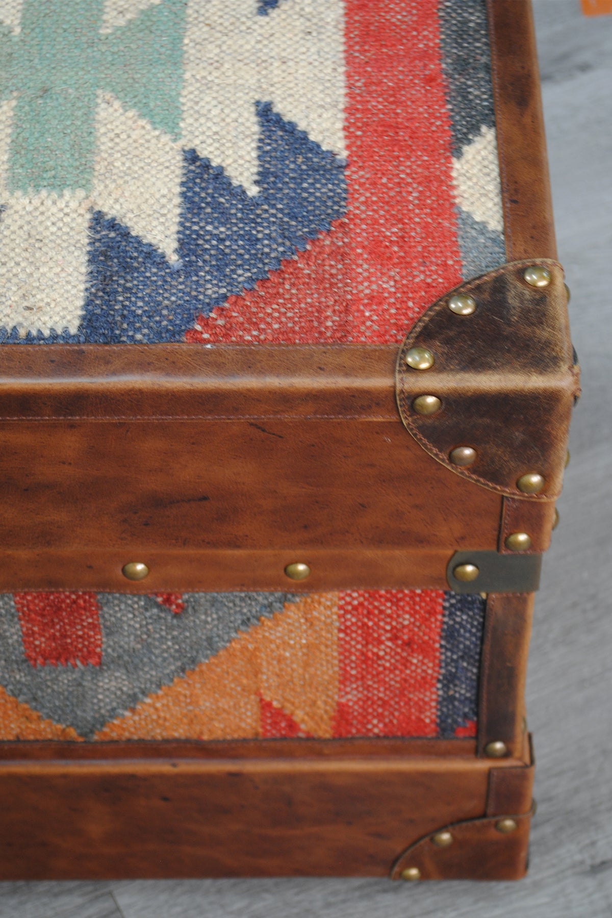 Detail of the kilim weave meeting the leather border and brass-studded corner cap