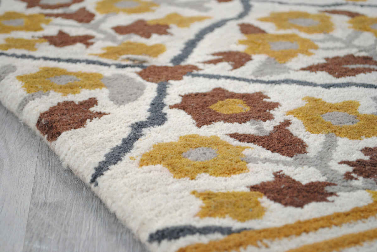Turned corner of the Sikandra rug showing the cut wool pile, charcoal lattice line and ivory wool-bound edge