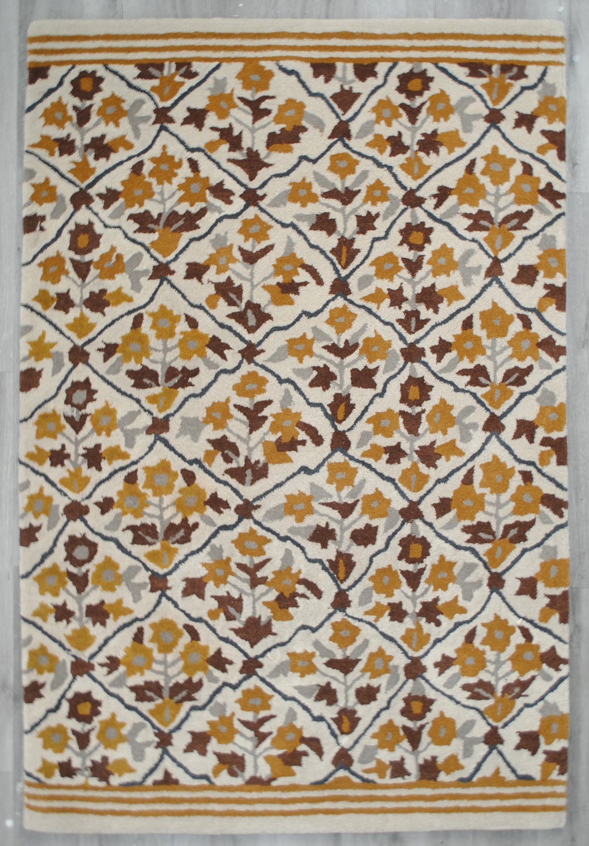 Sikandra hand-tufted rug laid flat on a grey wood floor, floral trellis on ivory