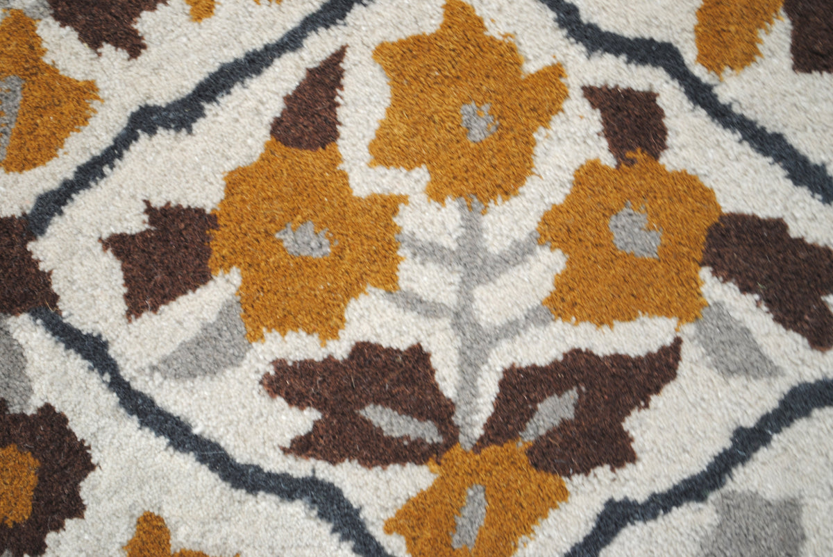 Close-up of one flowering plant on the Sikandra rug: ochre blossoms, brown leaves and a grey stem inside the charcoal lattice