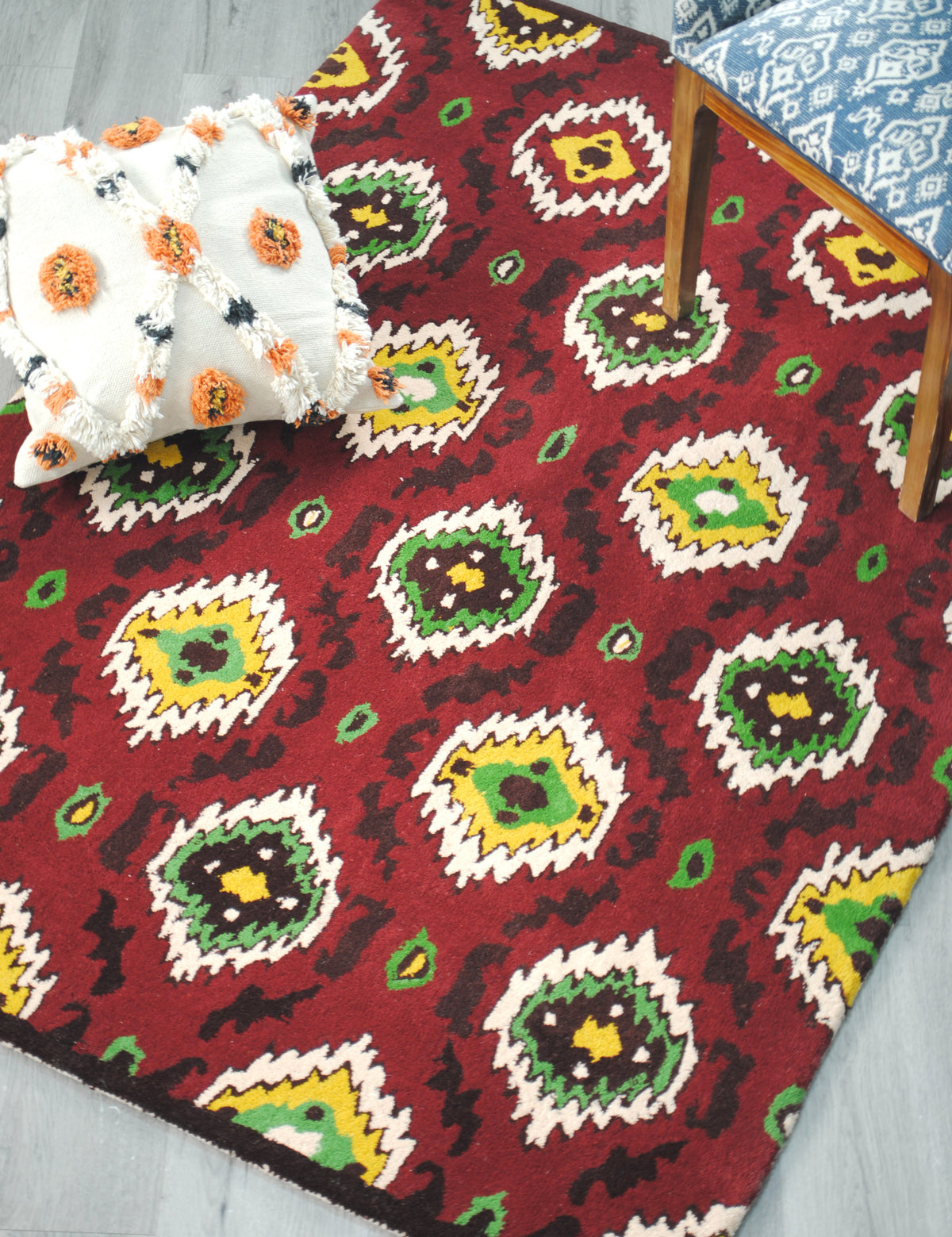 Sambalpur red ikat rug styled with a tufted ivory cushion and a wooden chair in blue ikat upholstery