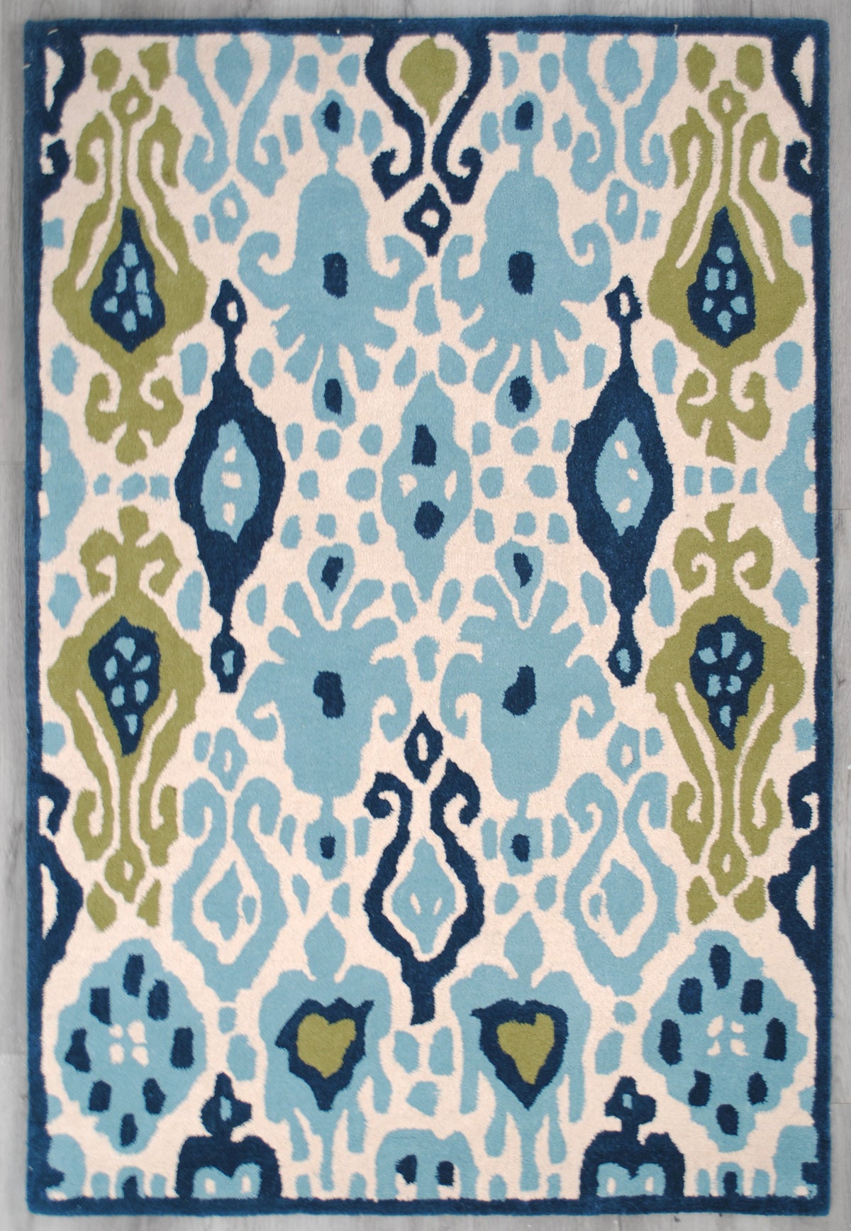 Pochampally ikat rug laid flat on a grey wood floor, blue and green on ivory