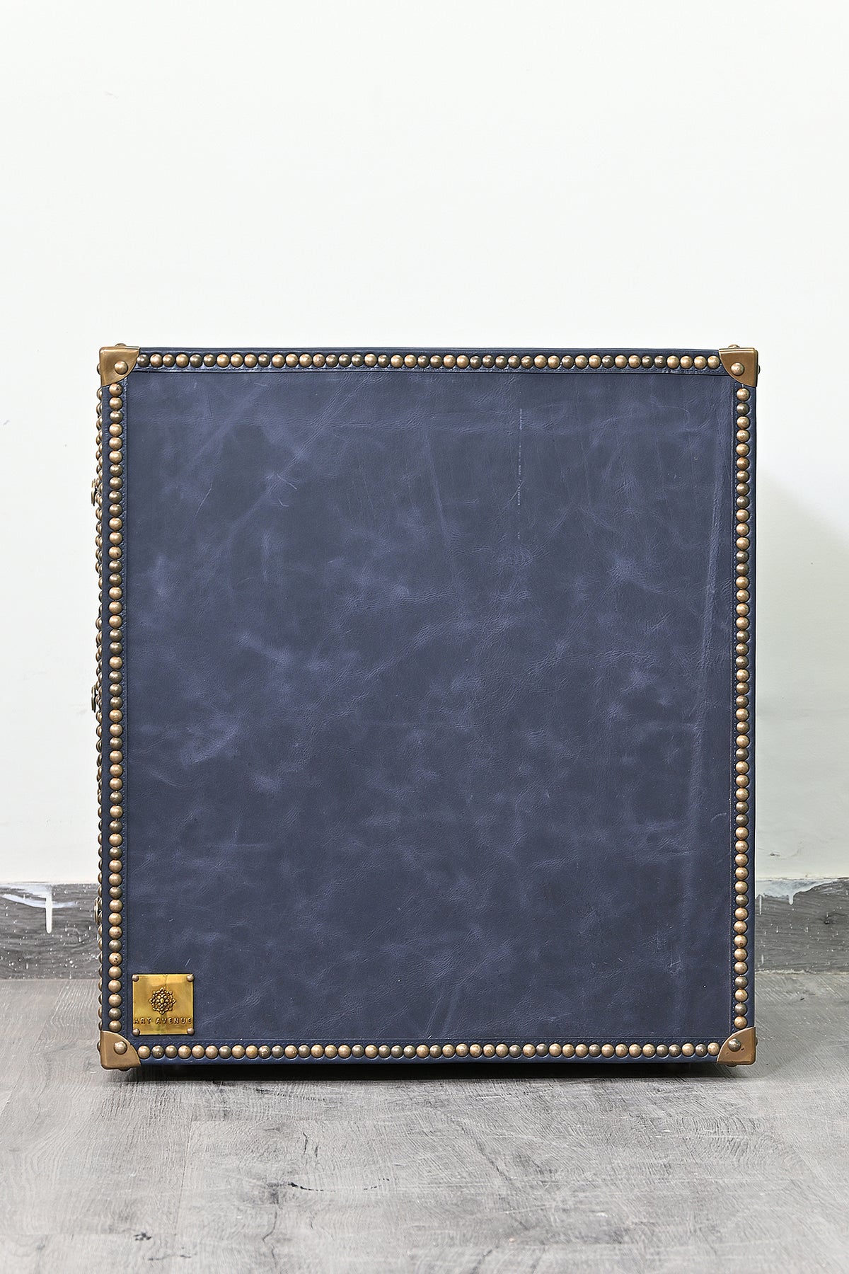 Side panel of the Samode bedside chest in plain navy leather framed by a brass stud border