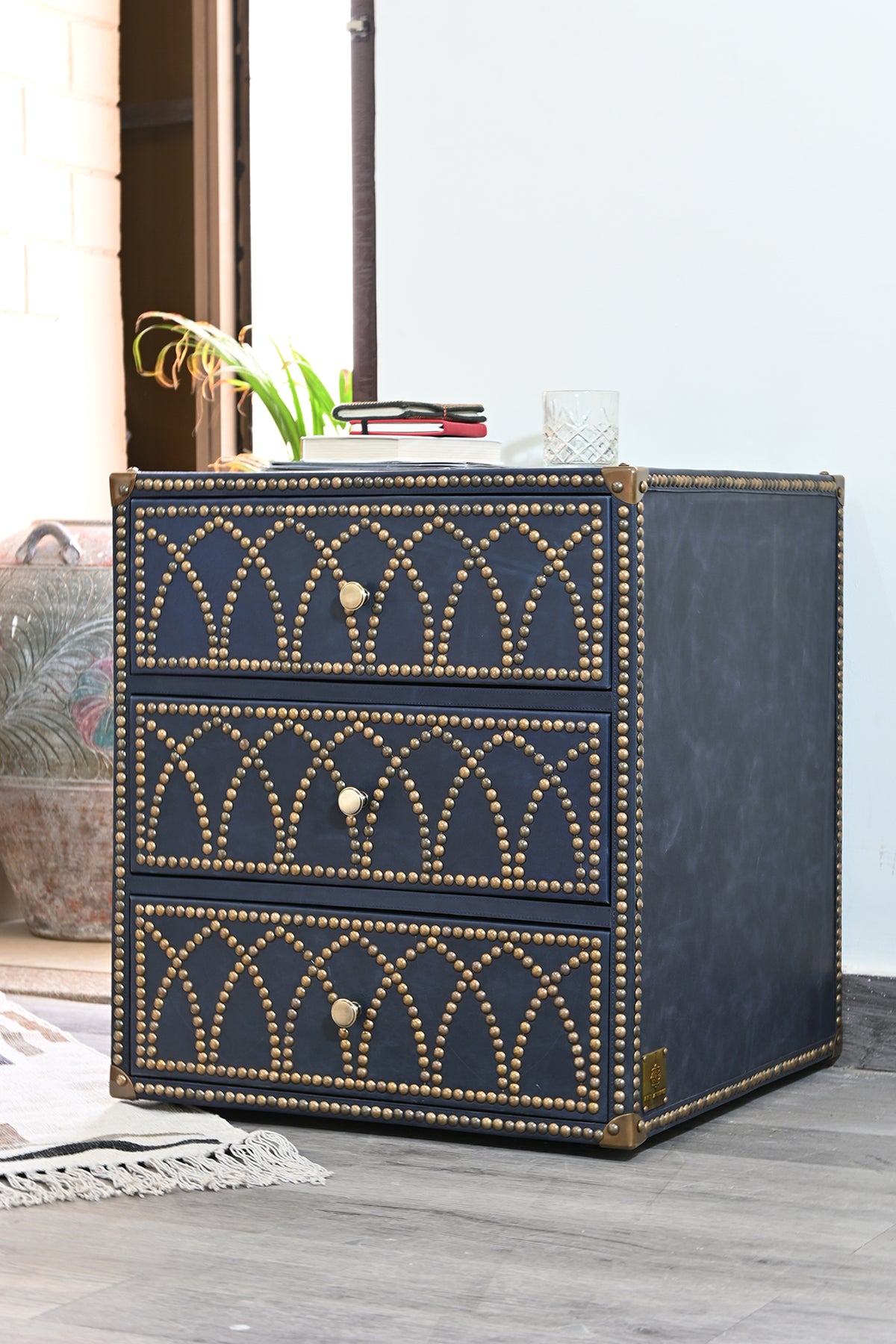 Samode bedside chest styled with books and a cut-glass tumbler beside a window