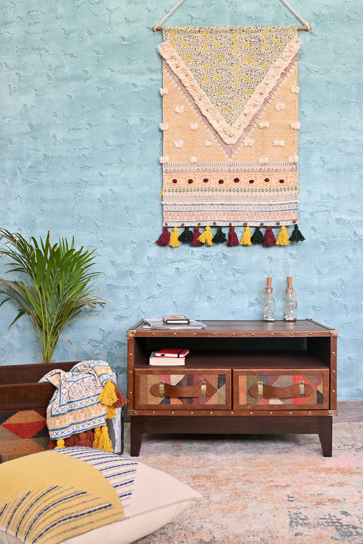 Barmer TV unit in a living room setting with floor cushions and a woven wall hanging