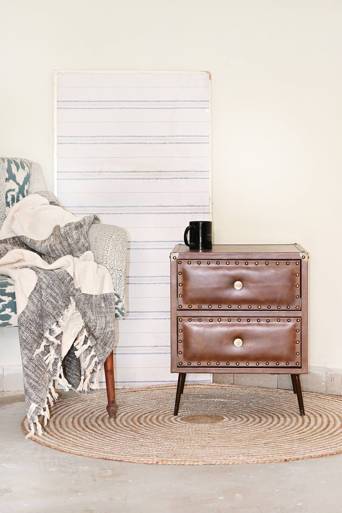 Kishangarh studded leather bedside table on a round jute rug beside an armchair, wide view, Art Avenue, made to order