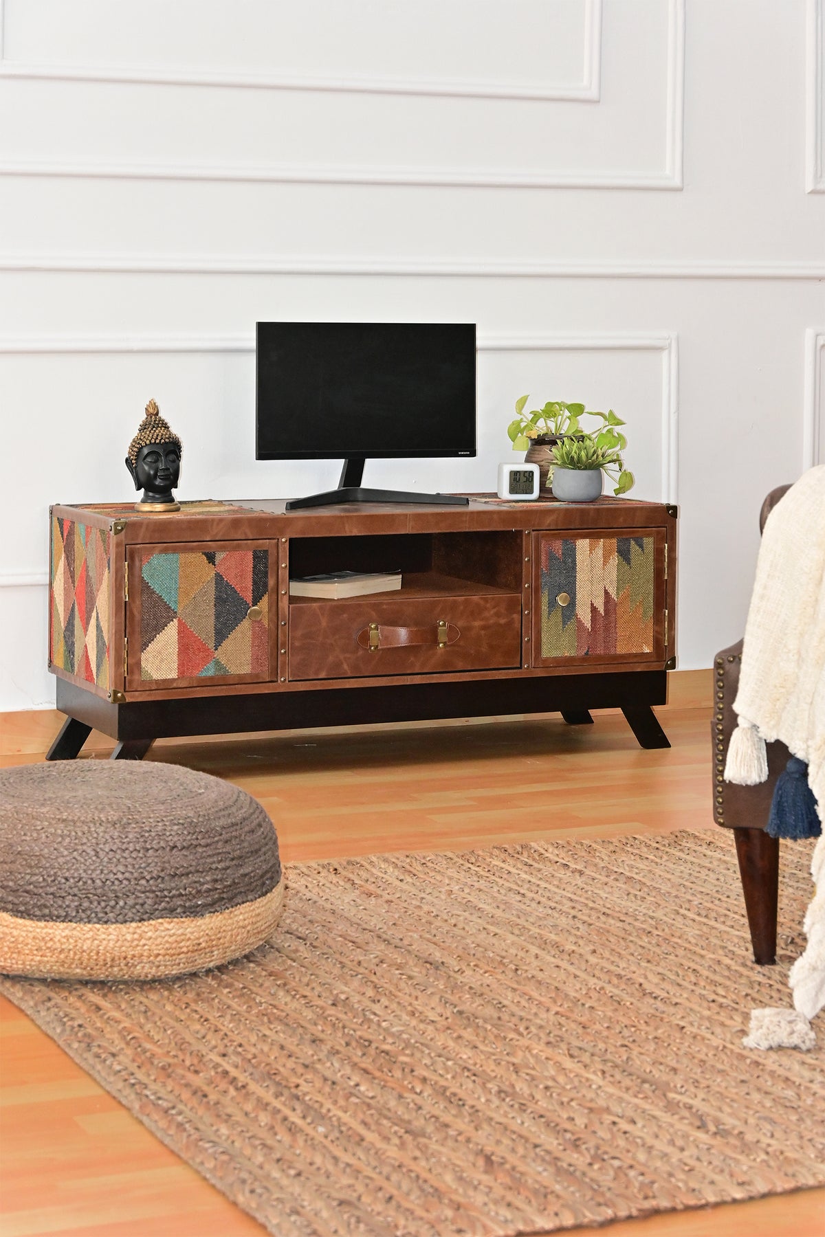 Karauli TV unit with a screen and plants on top, beside a jute rug and pouf