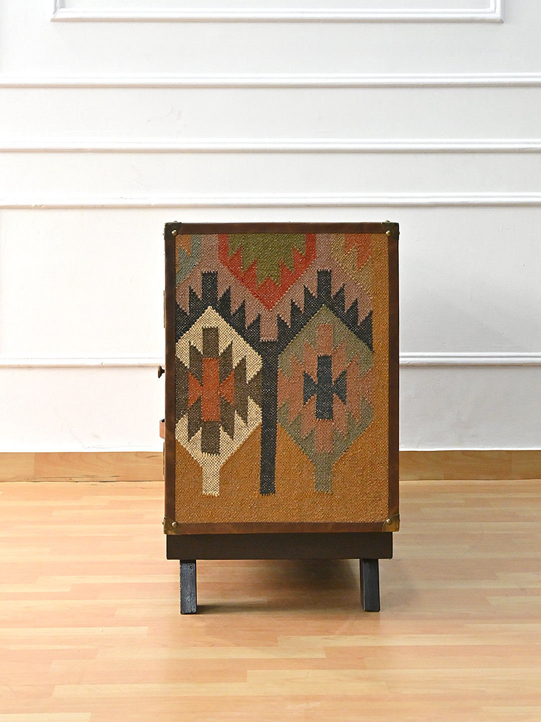 Side view of the Mukundgarh TV unit — full-height kilim panel framed in stitched leather with brass corners