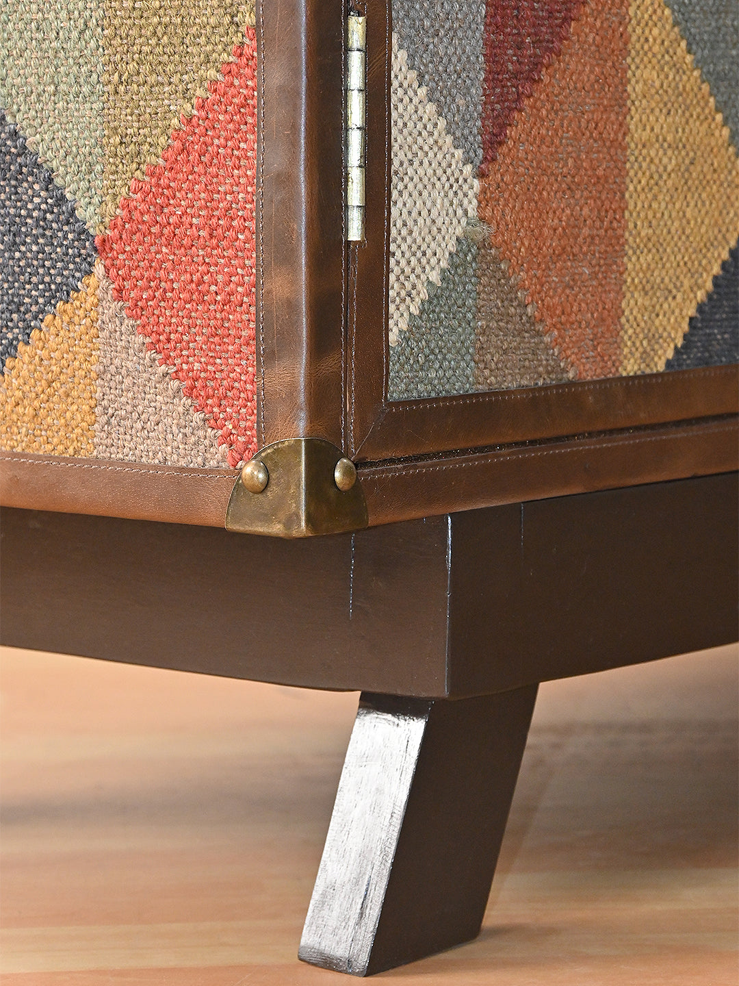 Detail of a kilim cupboard door with its stitched leather frame, hinge and a splayed solid wood leg
