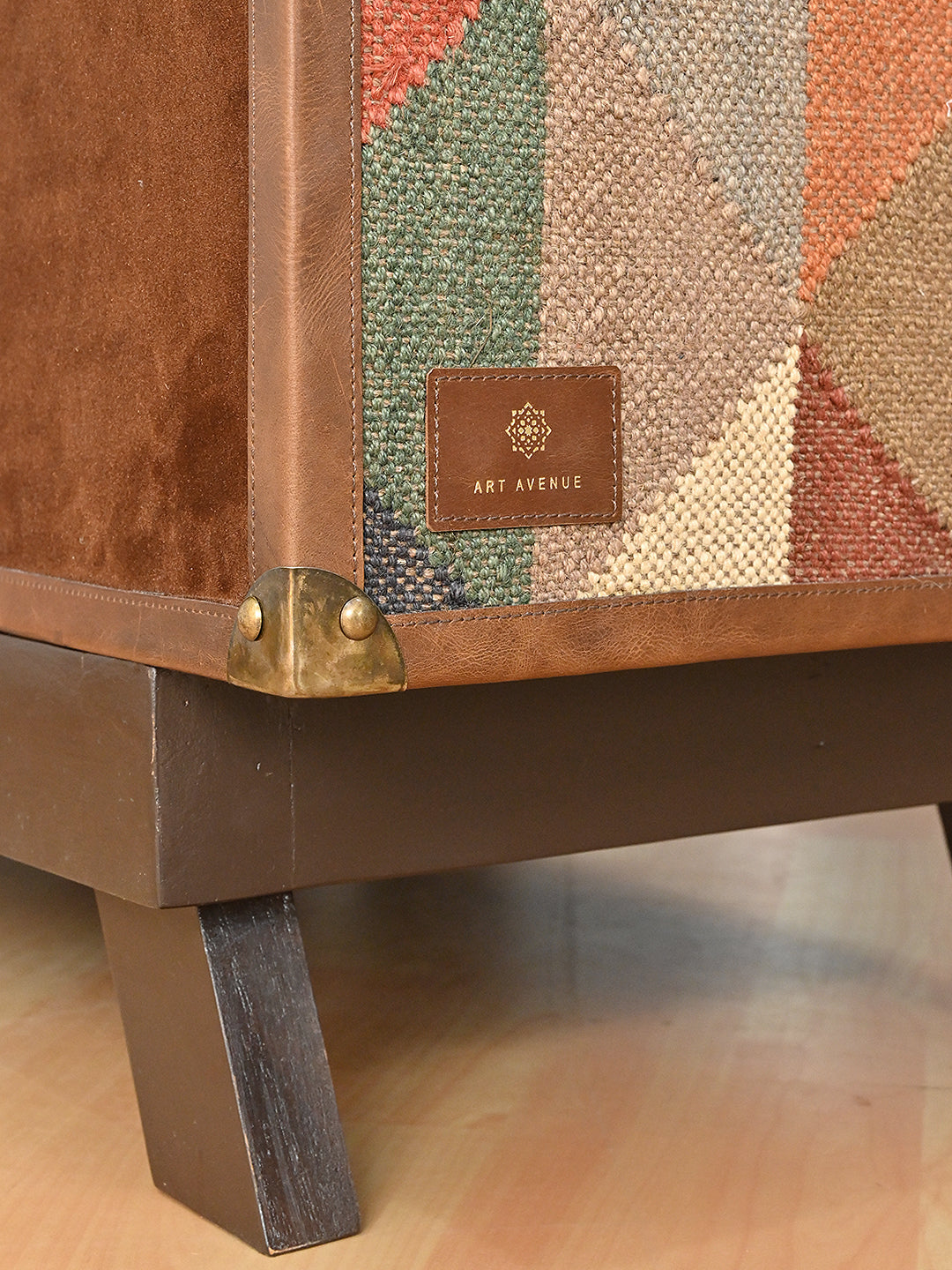 Embossed Art Avenue leather label on the kilim flank, above a brass corner cap and the solid wood plinth