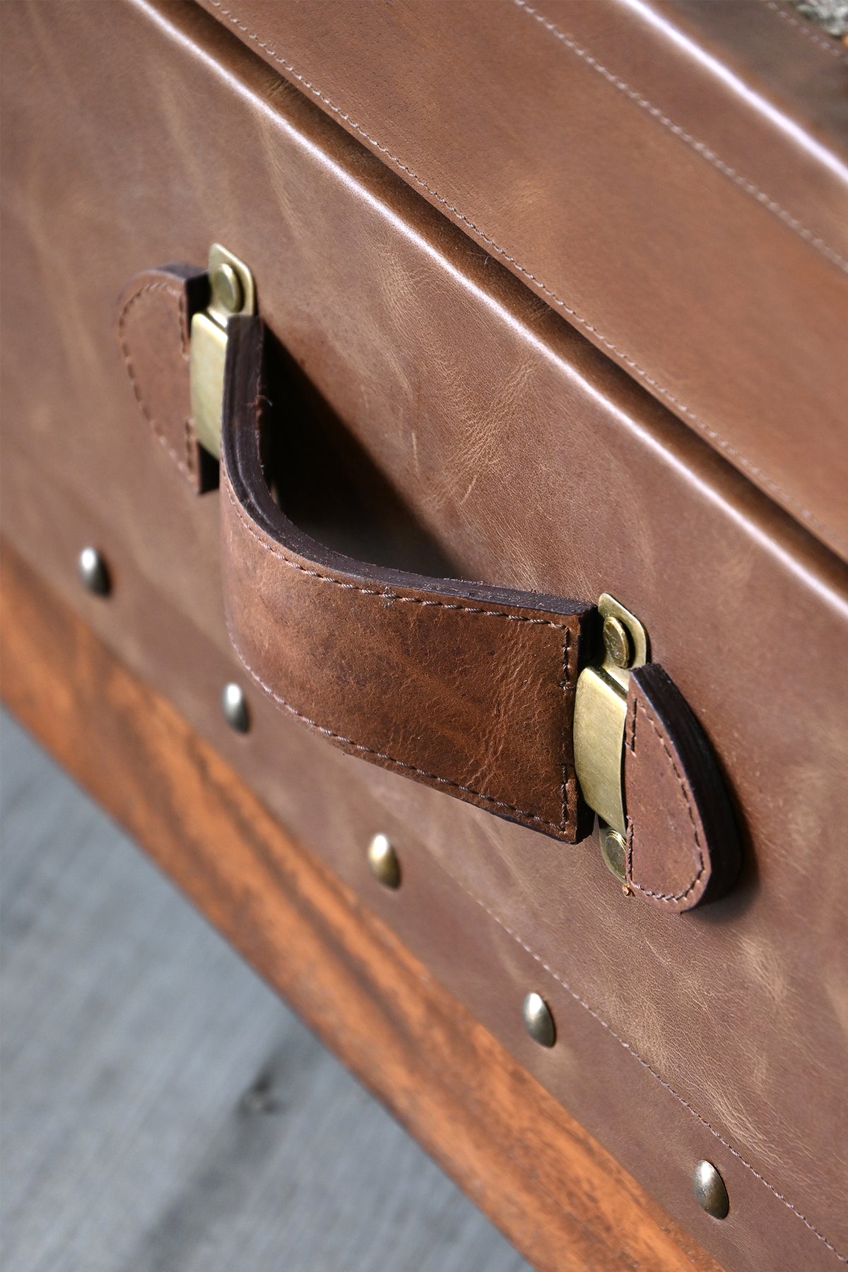 Macro detail of the saddle-stitched leather strap handle on shaped brass plates