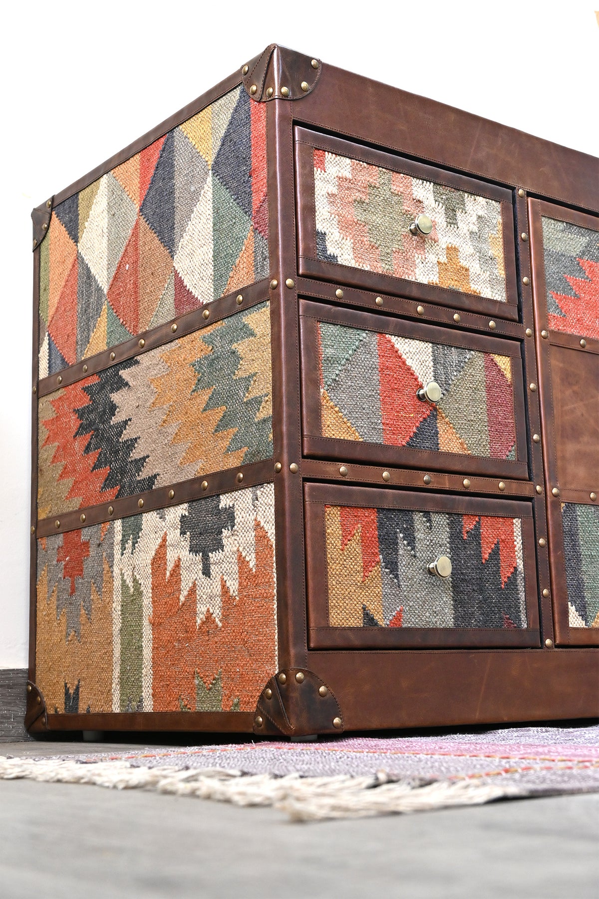 Low-angle view of the Nimaj sideboard's kilim side and three kilim drawers with brass knobs and stitched leather corner caps — Art Avenue