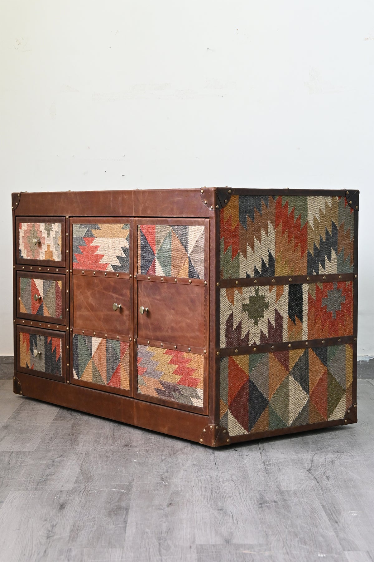 Three-quarter view of the Nimaj Kilim & Leather Sideboard showing kilim bands down the side, divided by brass-studded leather straps — Art Avenue