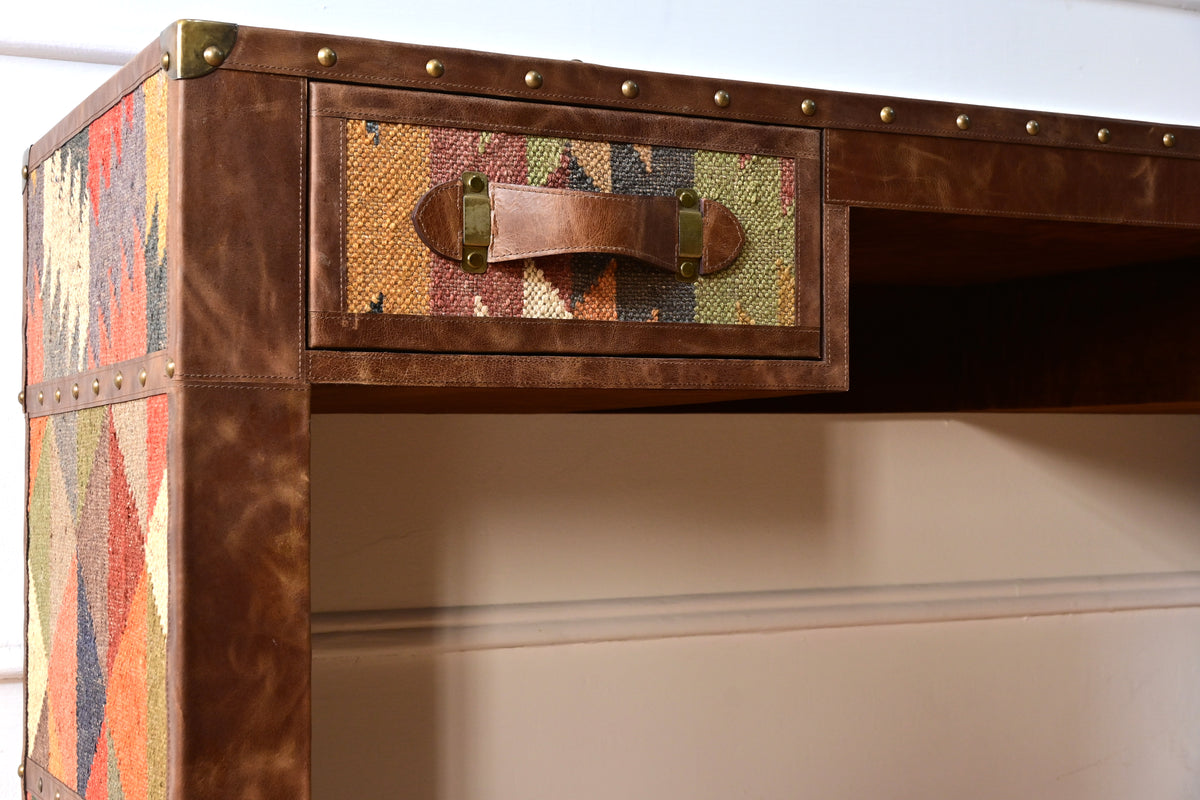 Close-up of a kilim drawer front with a stitched leather strap handle on brass mounts